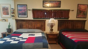A bedroom with two beds, a nightstand, a lamp, and framed pictures on the wall. - The Lazy Ass Ranch. The National Parks Room (Panguitch)