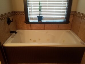 Une baignoire rectangulaire avec un robinet situé à gauche, une fenêtre avec des stores et une plante en pot placée au-dessus, et des murs carrelés avec une bordure décorative.