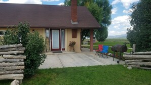 A house with a red roof, a brick chimney, and a front porch with two folding chairs and a barbecue grill. - The Lazy Ass Ranch. The National Parks Room (Panguitch)