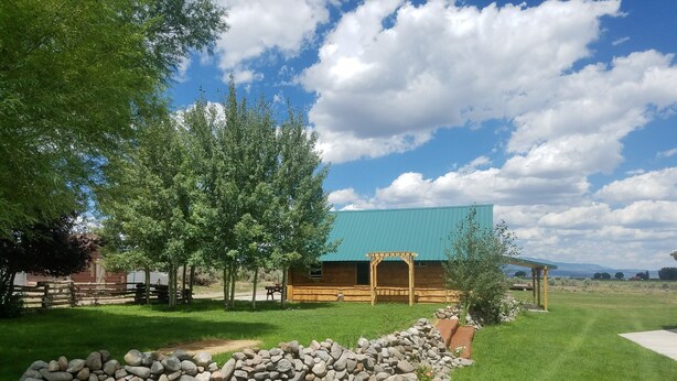 A rustic cabin with a green roof, surrounded by a well-maintained lawn and a stone wall. - The Lazy Ass Ranch. The National Parks Room (Panguitch)