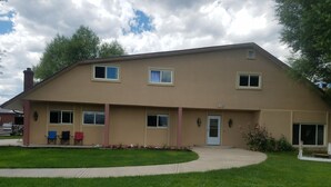 A two-story building with a beige exterior, numbered 2193, featuring a front porch with outdoor seating and a well-maintained lawn. - The Lazy Ass Ranch. The National Parks Room (Panguitch)