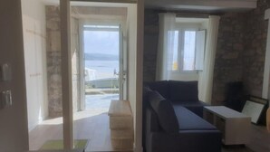 Un salon avec un canapé, une petite table et une vue sur la mer, visible à travers une porte vitrée.