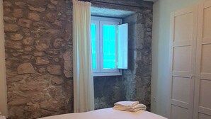 Une chambre avec un mur en pierre, une fenêtre avec des rideaux, un lit et une pile de serviettes.