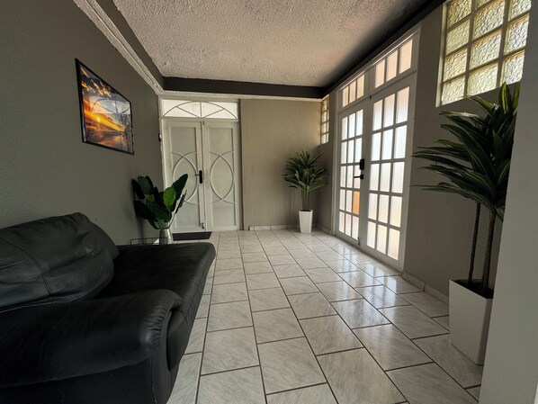 A spacious hallway with a black leather sofa, a potted plant, and a large window with decorative glass panes.