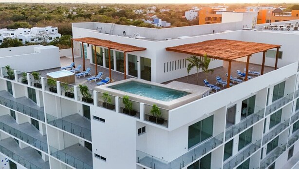 A modern hotel rooftop with a swimming pool, sun loungers, and a view of the cityscape.