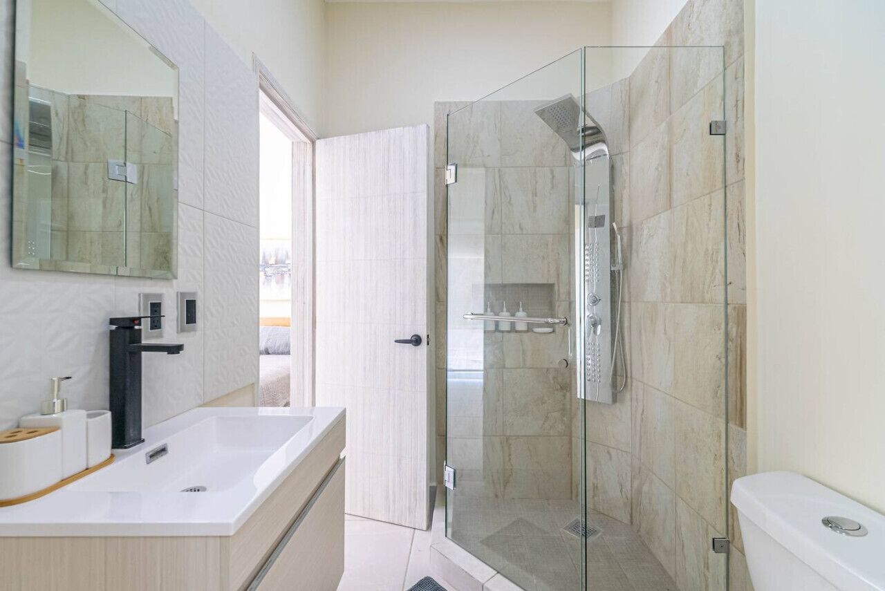 Un baño moderno con cabina de ducha de vidrio, un lavabo blanco y un espejo grande.