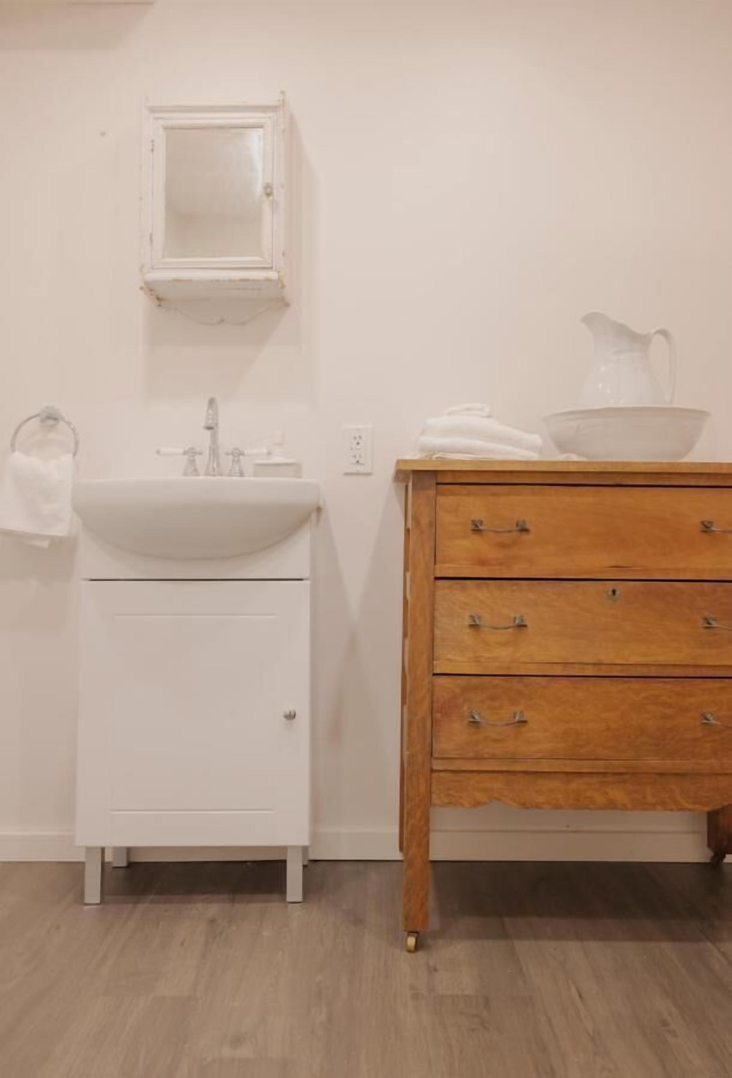 Un baño con un lavamanos blanco, un mueble de madera con cajones y un espejo sobre el lavamanos.