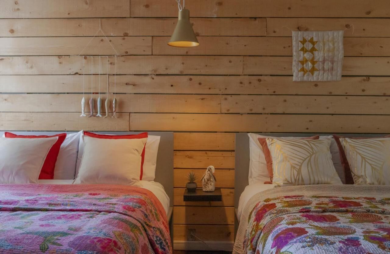 Una habitación con dos camas, paredes de madera, una lámpara colgante y un estante con un adorno.