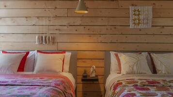Una habitación con dos camas, paredes de madera, una lámpara colgante y un estante con un adorno.