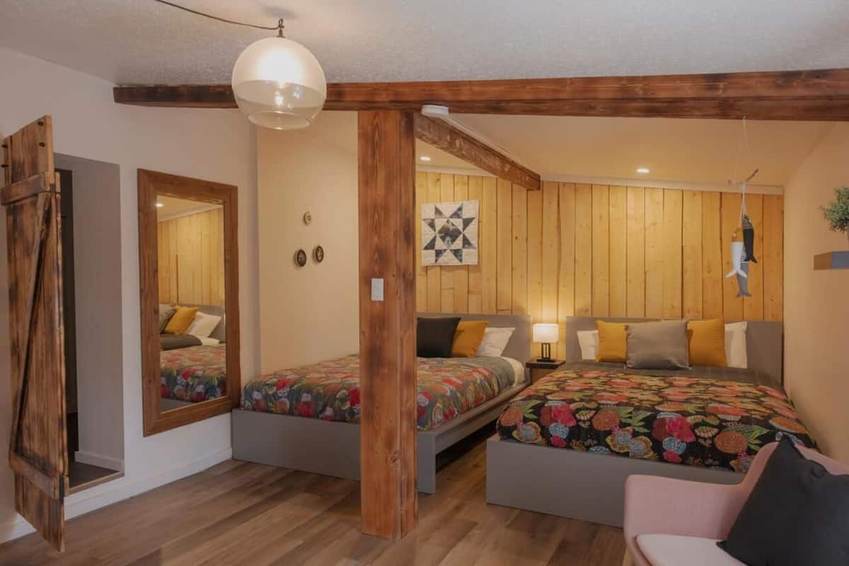 A bedroom with two single beds, a wooden ceiling, a mirror, and a hanging light fixture.