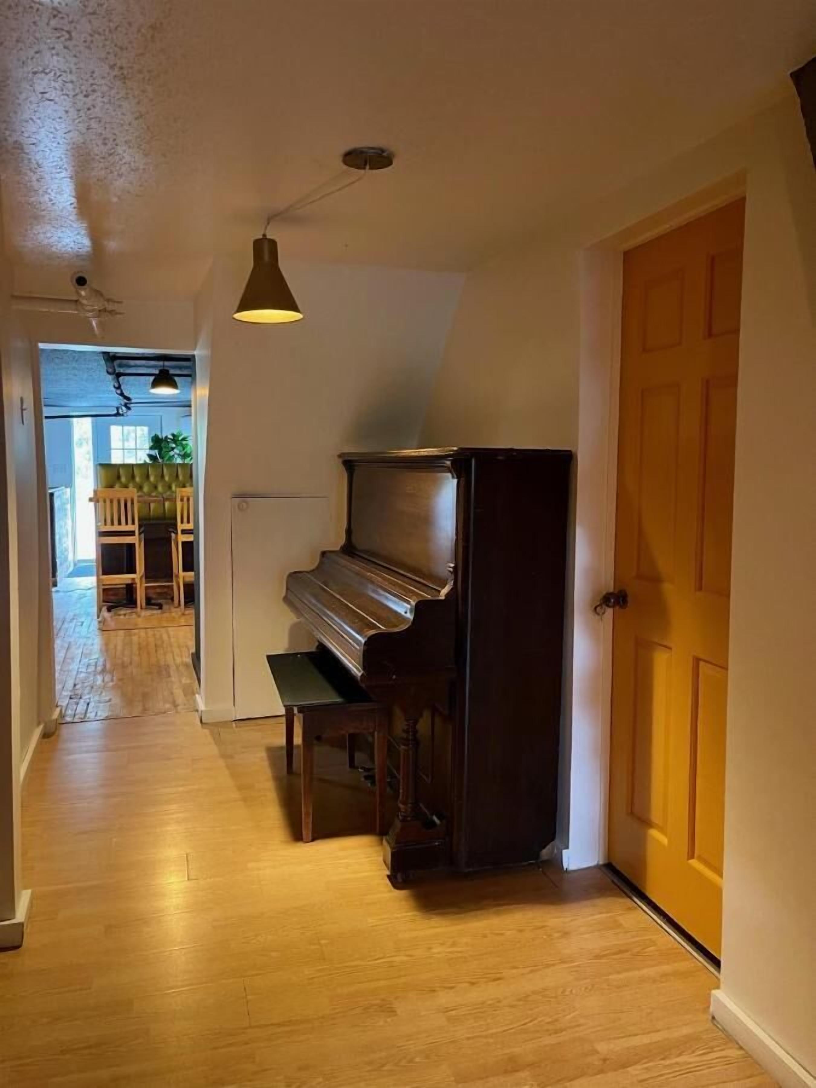 A hallway with a grand piano, wooden flooring, and a door on the right.
