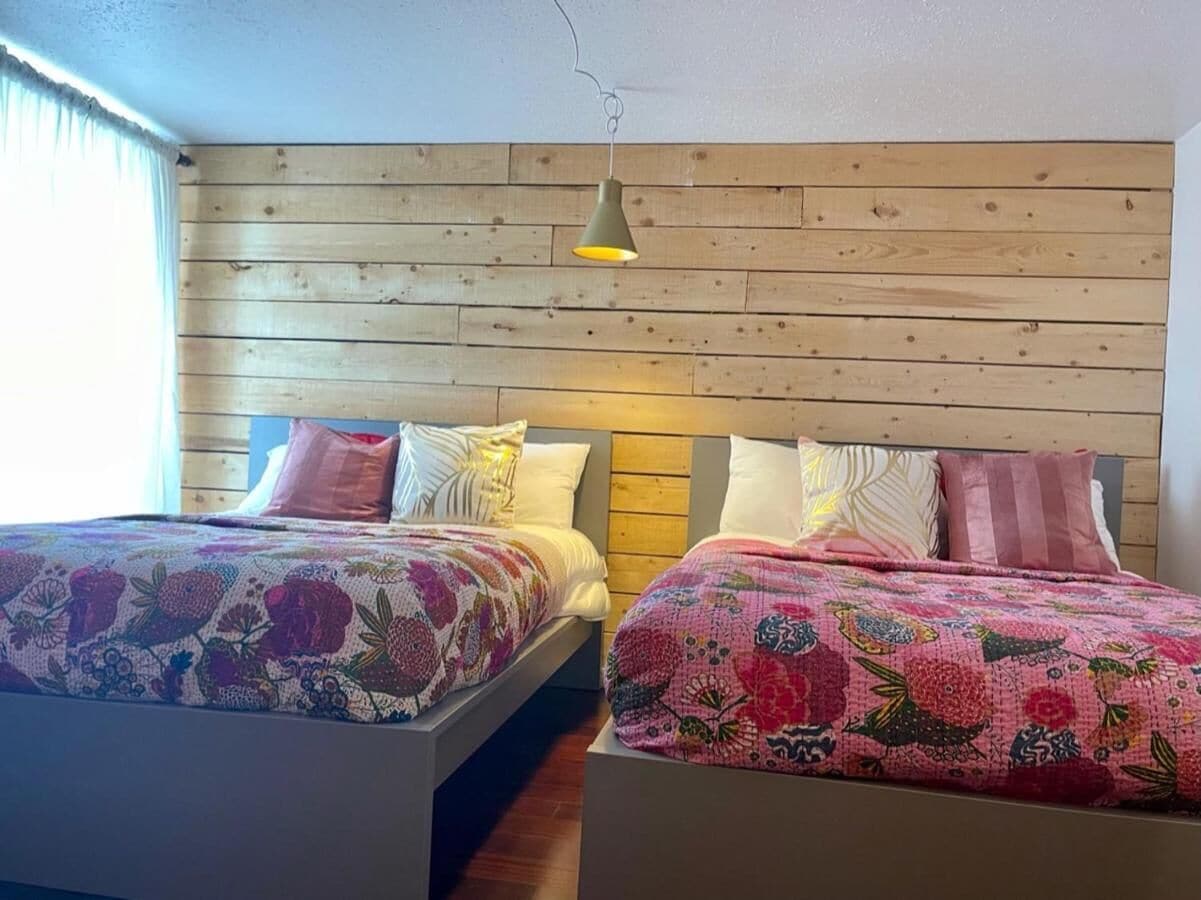 A room with two beds, each with floral-patterned bedding, wooden headboards, and a hanging light fixture.