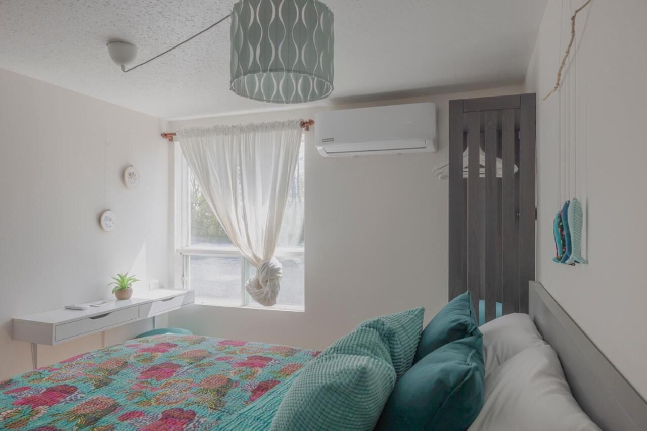 Un dormitorio con cama, escritorio, ventana con cortinas, unidad de aire acondicionado y un mueble en la pared con toallas.