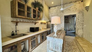 Una cocina con encimera de madera, un fregadero, un microondas y una estufa. Hay un ventilador de techo y una alfombra estampada en el suelo.