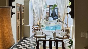 Una habitación con piso a cuadros, una mesa con sillas, una lámpara colgante y vistas a una zona de piscina al aire libre.