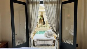 Un dormitorio con cama, una mesita y vistas a una piscina y zona de estar exterior a través de un ventanal.