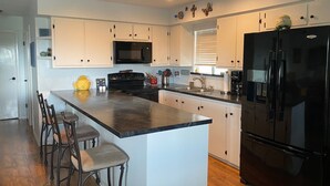 A modern kitchen with white cabinets, a black refrigerator, and a granite countertop. - Charming 2-bedroom waterfront house with dock, AC, and WiFi in Rockport Texas (Rockport)
