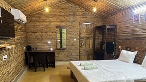 Una habitación con cama, escritorio, silla, paredes de bambú y ventilador de techo.