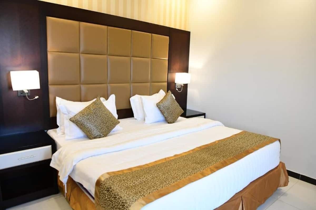 A hotel room with a large bed, two bedside tables, and a headboard with a light fixture.