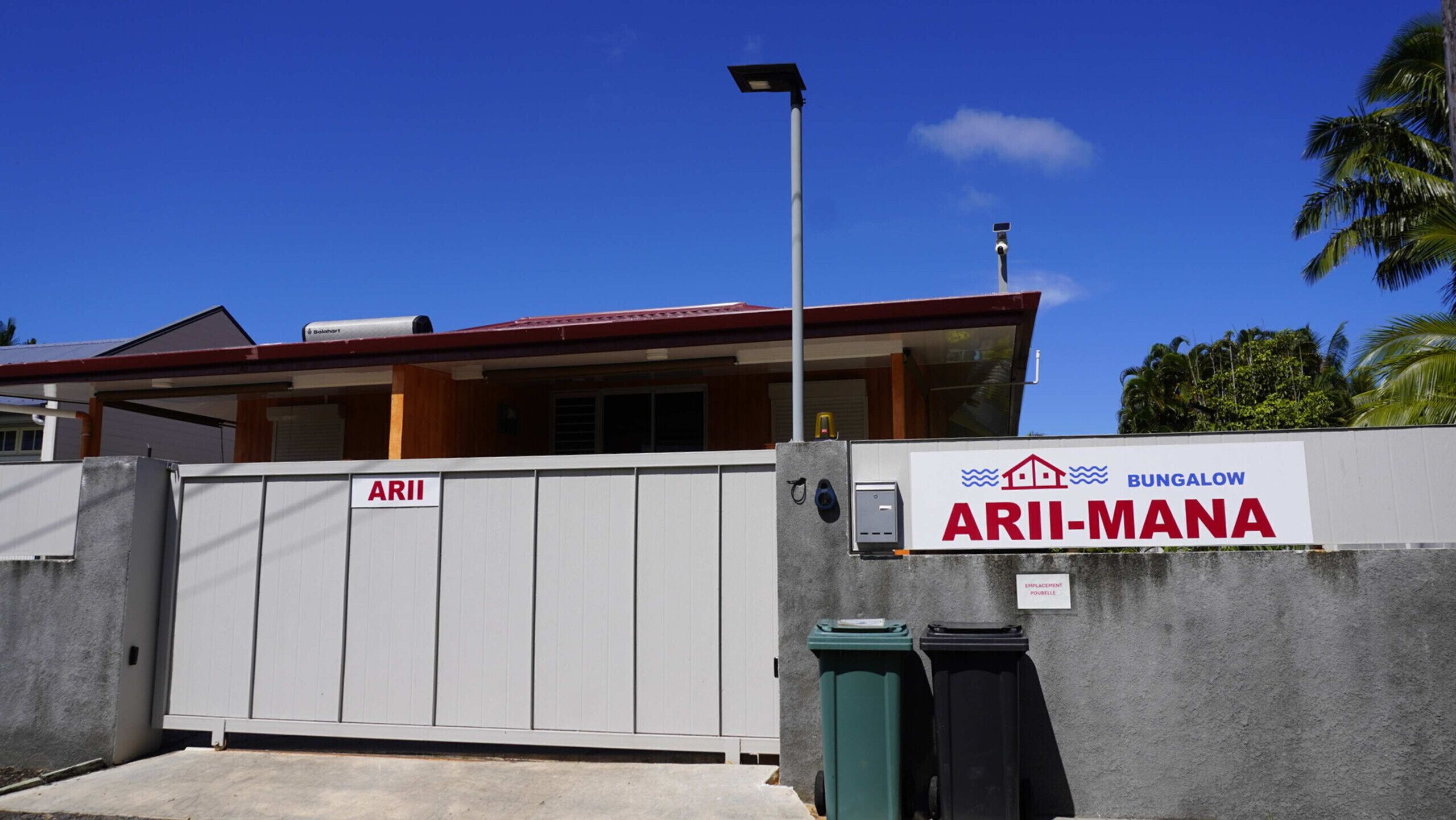 A gated entrance with a sign reading 'ARI-MANA' and a solar panel on a pole.