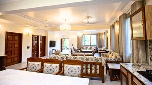 A spacious living room with a large marble table, comfortable seating, and a chandelier.