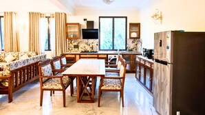 A spacious kitchen with a dining area, marble flooring, wooden furniture, and a modern refrigerator.