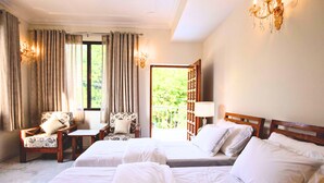 A hotel room with two beds, a chair, a small table, and a chandelier.