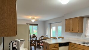 Una cocina con armarios de madera, lavavajillas, cafetera y comedor con sillas y mesa.