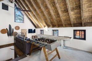 Una habitación con mesa de fútbol, vigas de madera en el techo y un televisor montado en la pared.