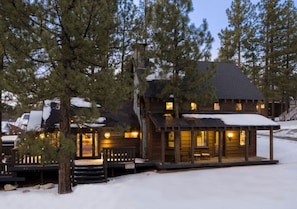 A wooden cabin with a porch, a covered outdoor seating area, and a snow-covered roof.