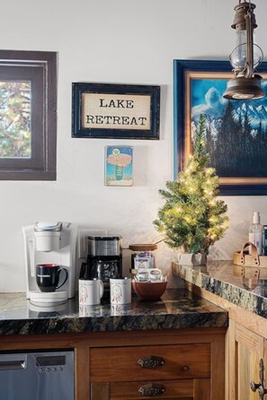Una cocina con cafetera, tazas, un pequeño árbol de Navidad y un cartel enmarcado que dice 'LAKE RETREAT'.