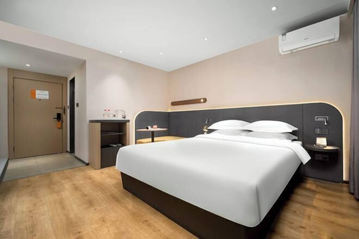 A modern hotel room with a large bed, bedside tables, a desk, and an air conditioning unit.