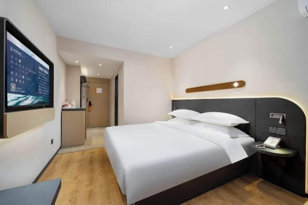 A modern hotel room with a large bed, a bedside table with a phone, and a TV mounted on the wall.