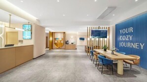 A modern hotel lobby with a reception desk, a seating area with a long table, and a wall with the text "YOUR COZY JOURNEY". - Jinjiang Inn Hotel (Zhengzhou Ocean Park Wenhua Road Branch) (Zhengzhou)