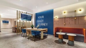 A modern hotel lobby with a dining area, a seating area with round tables, and a large blue wall with the text "YOUR COZY JOURNEY". - Jinjiang Inn Hotel (Zhengzhou Ocean Park Wenhua Road Branch) (Zhengzhou)