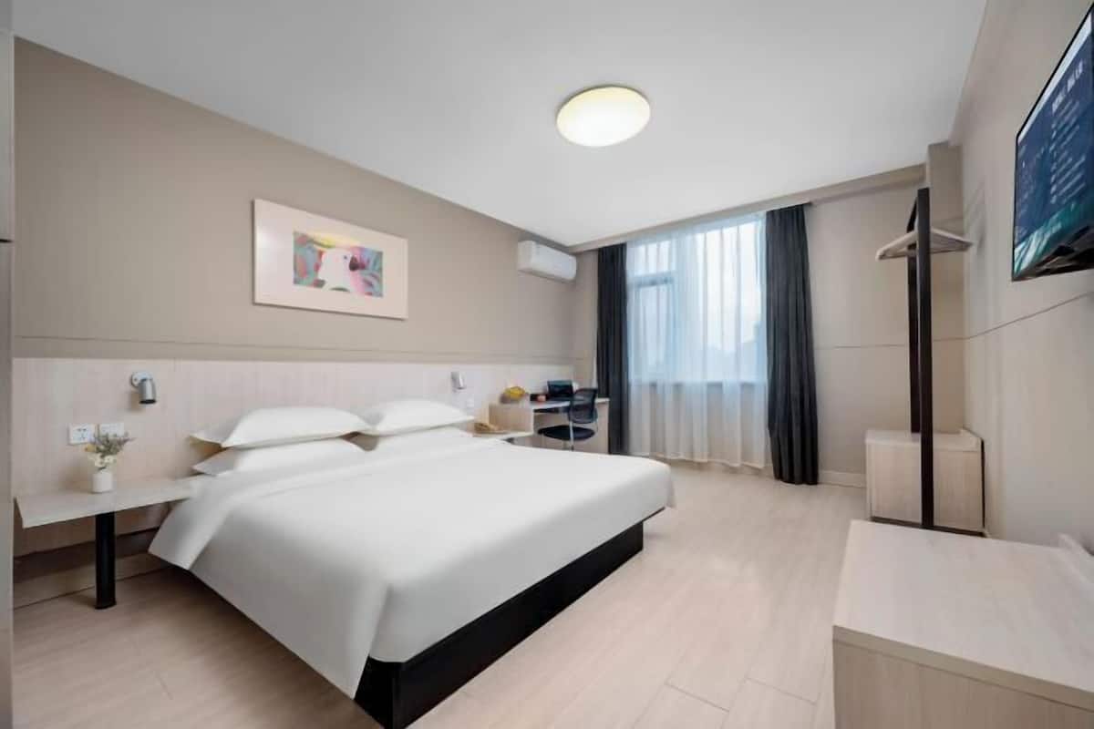 A modern hotel room with a large bed, bedside tables, a desk, and a flat-screen TV.