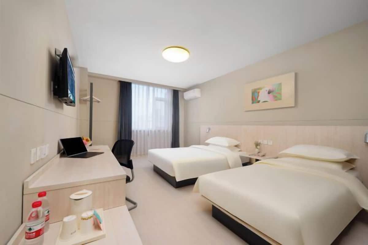 A hotel room with two beds, a desk with a laptop, a chair, and a TV mounted on the wall.