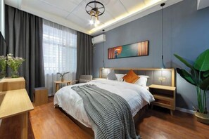 A modern hotel room with a large bed, wooden flooring, a ceiling light fixture, a wall-mounted air conditioner, and a large window with curtains.
