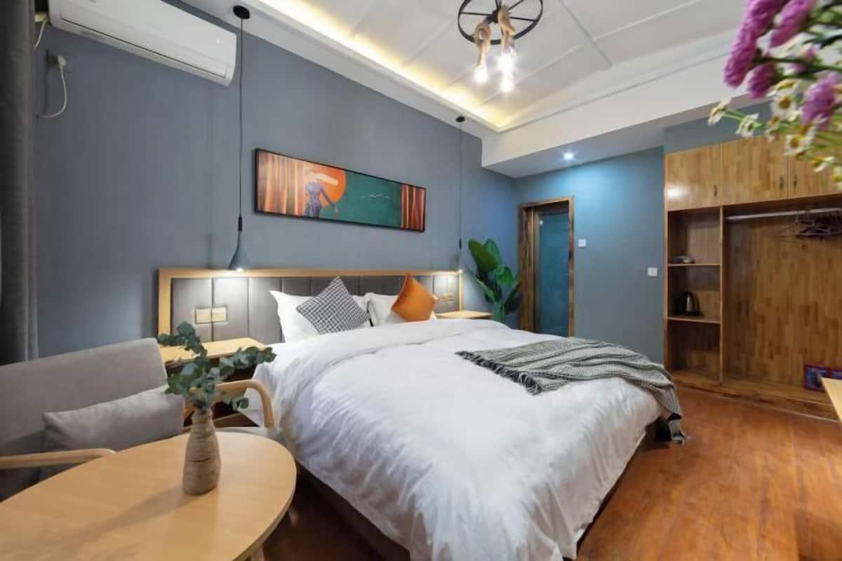 Habitación de hotel moderna con una cama grande, un armario de madera, un escritorio con un florero y un cuadro en la pared.