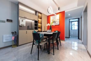 A modern dining area with a table and chairs, a kitchen area with cabinets and appliances, and a bright red accent wall.