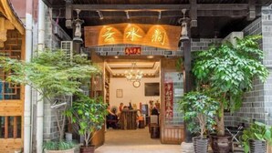 Entrada de un restaurante chino tradicional, con un letrero, plantas en macetas y decoración de madera.