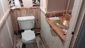 A small, compact bathroom with a toilet, a wooden vanity, and a sink.