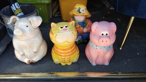 Three ceramic pig figurines on a dark surface.