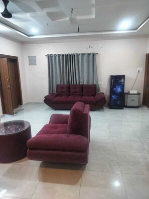 A living room with a sofa, ottoman, and a refrigerator. - NC Homestays (Tirupati)