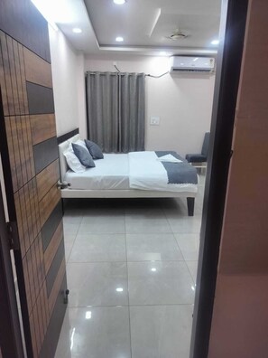 A bedroom with a bed, curtains, an air conditioning unit, and a tiled floor. - NC Homestays (Tirupati)