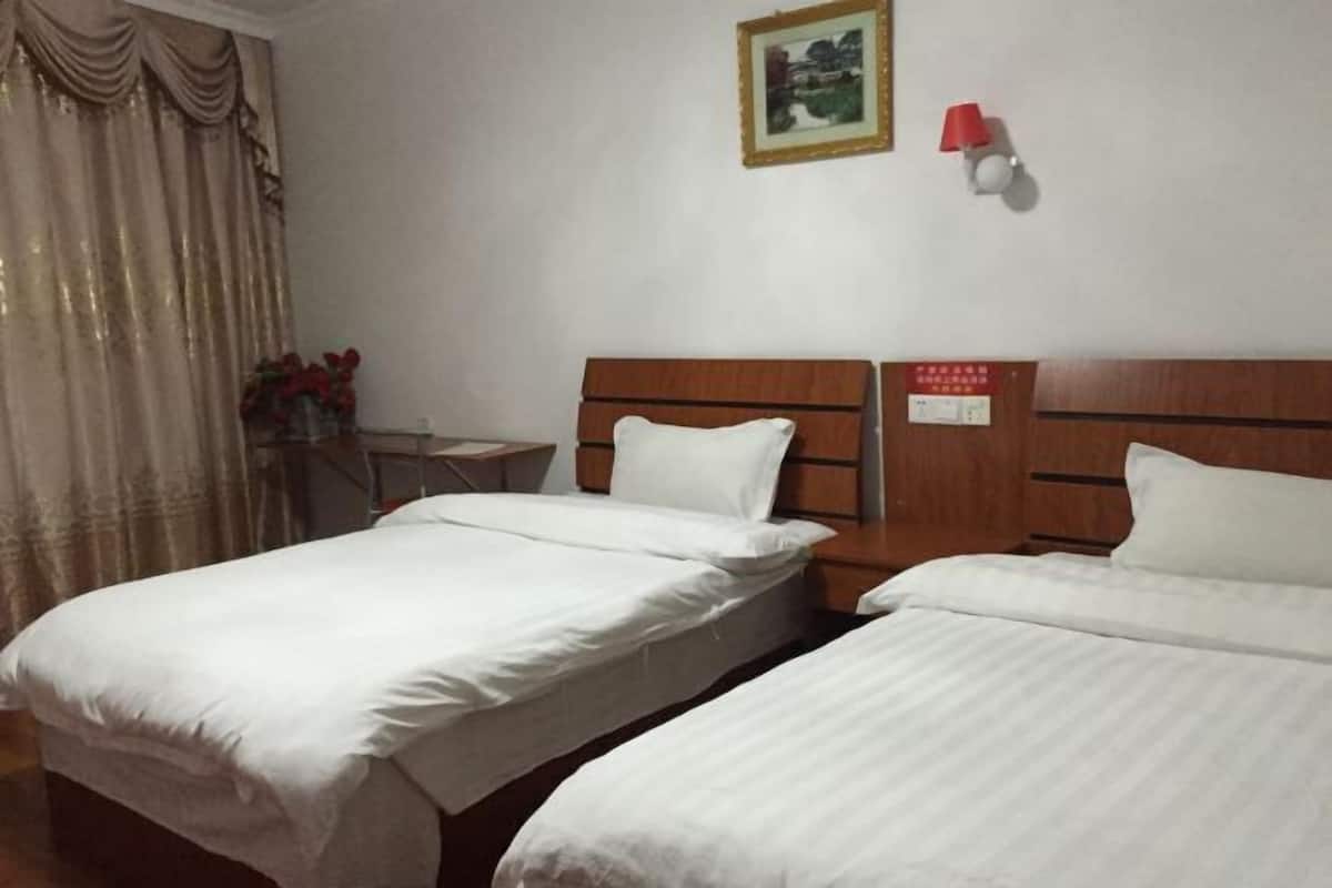 A hotel room with two single beds, a nightstand, a lamp, and a framed picture on the wall.