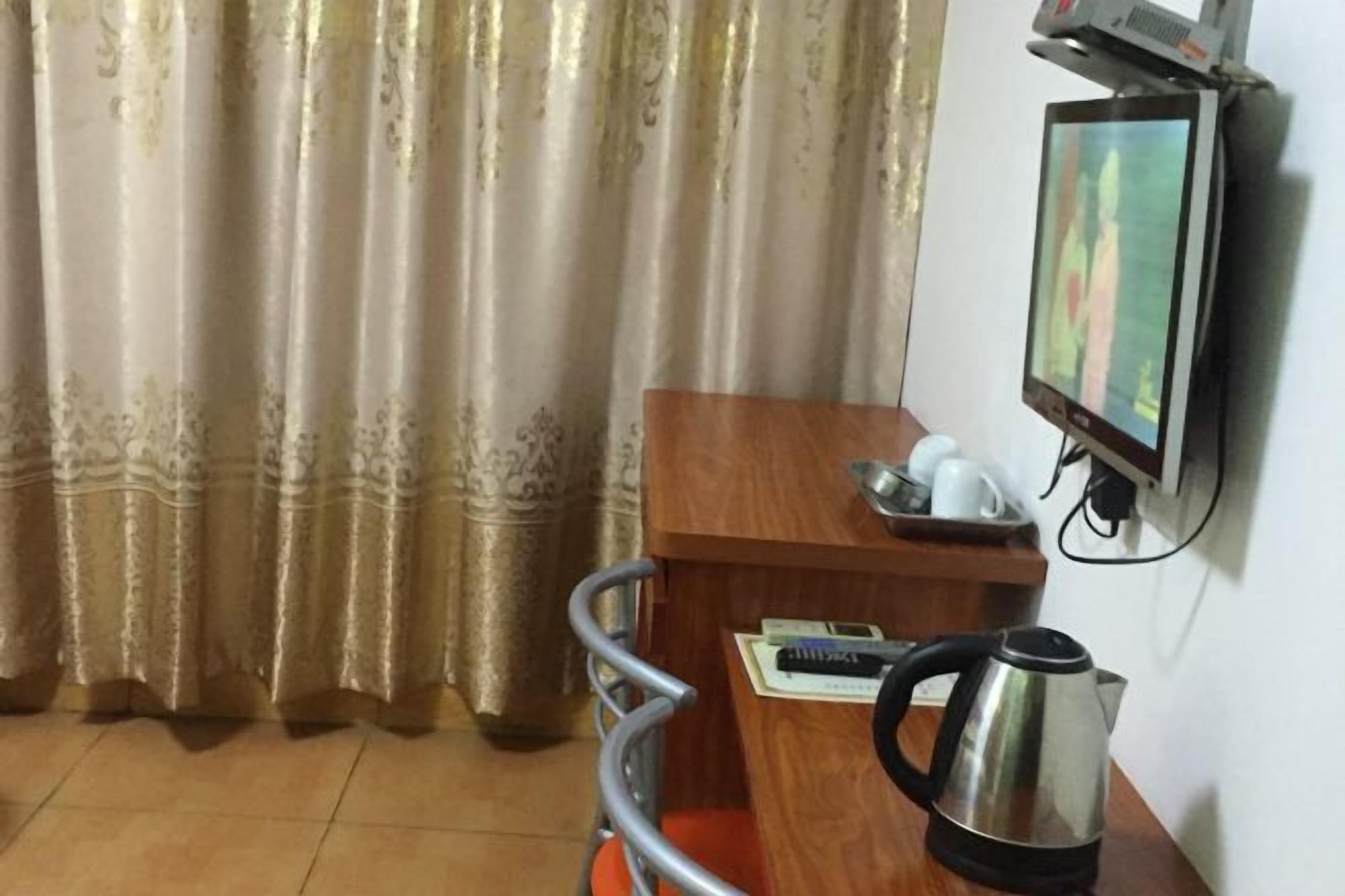 Habitación de hotel con un escritorio de madera, una tetera, un televisor montado en la pared y una cortina.