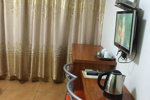 A hotel room with a wooden desk, a kettle, a television mounted on the wall, and a curtain. - Longyan Jinyuan Hotel (Longyan)