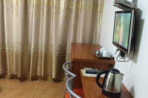 Quarto de hotel com escrivaninha de madeira, chaleira, televisão fixada na parede e cortina.