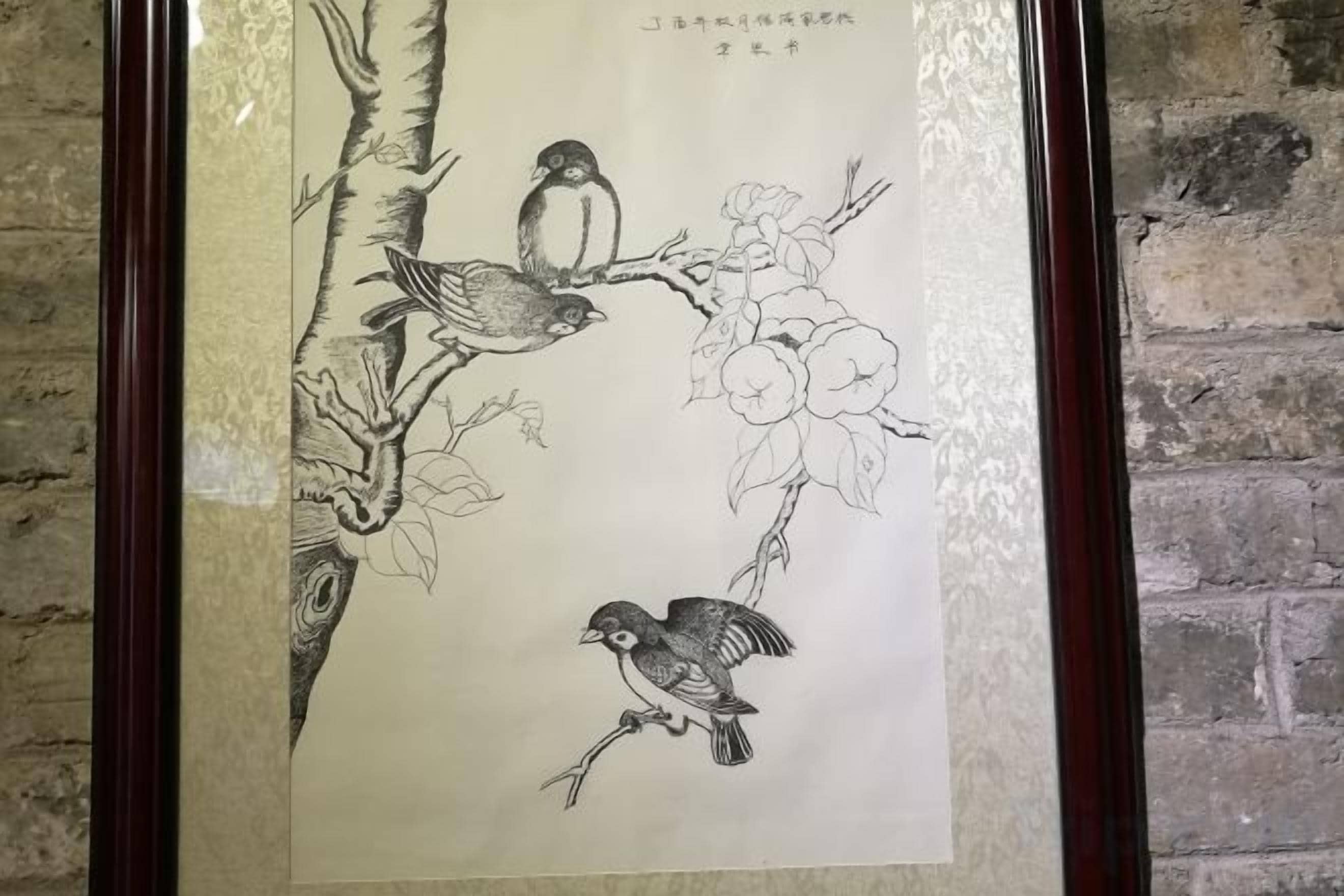 A framed artwork of birds on a branch with flowers.